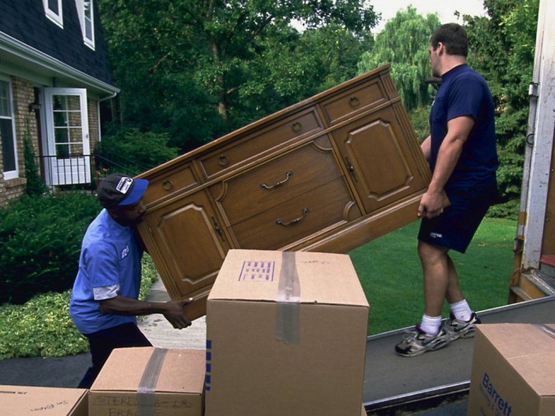 Two movers carefully carrying a heavy furniture into their moving truck