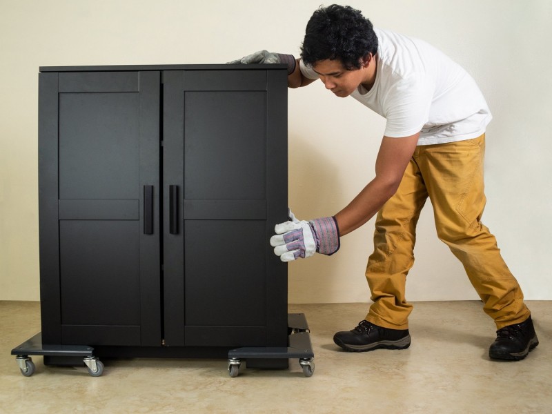 A mover pushing a moving dolly with a cabinet on it